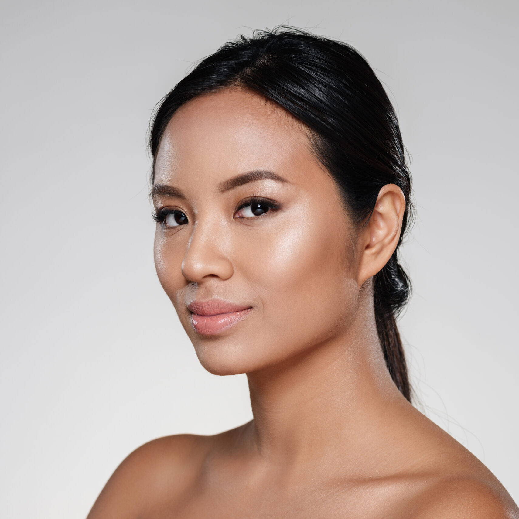 Beauty portrait of an attractive half naked asian woman looking at camera isolated over gray background